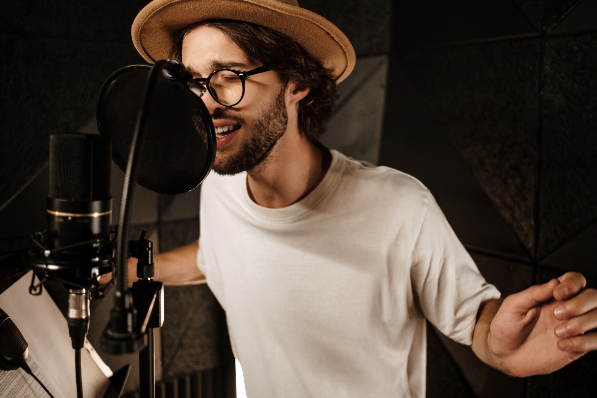 Handsome stylish male musician emotionally singing in microphone recording song in studio
