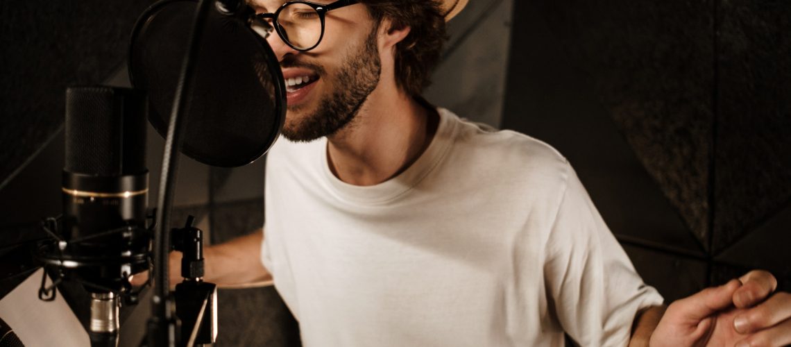 Handsome stylish male musician emotionally singing in microphone recording song in studio